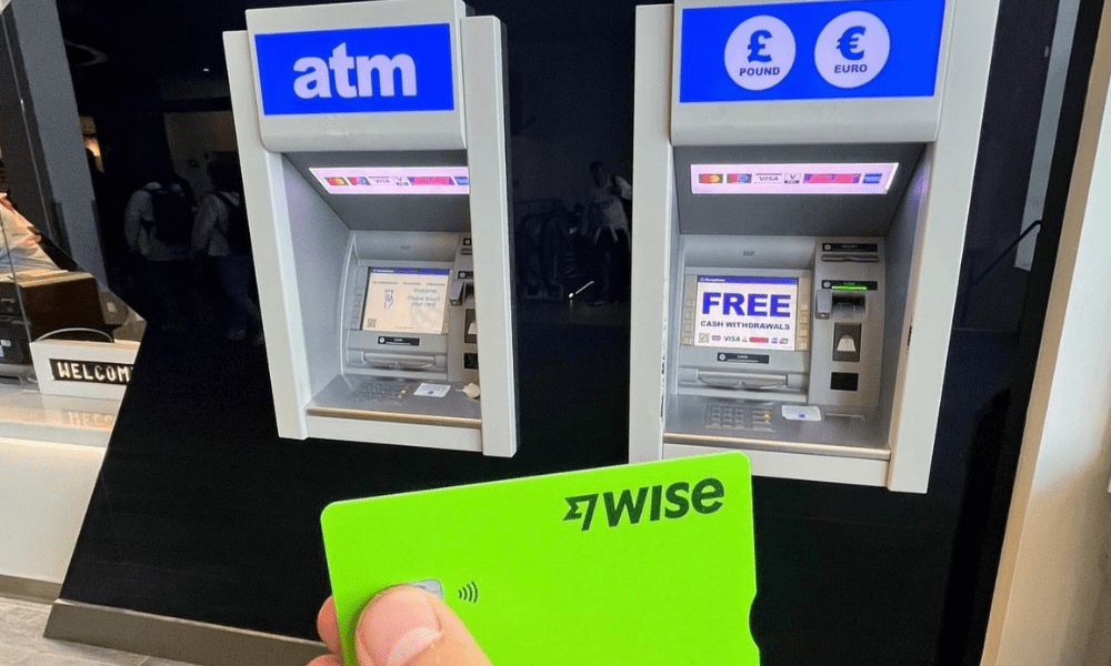 This is an image of someone holding a Wise card in front of two ATMs.