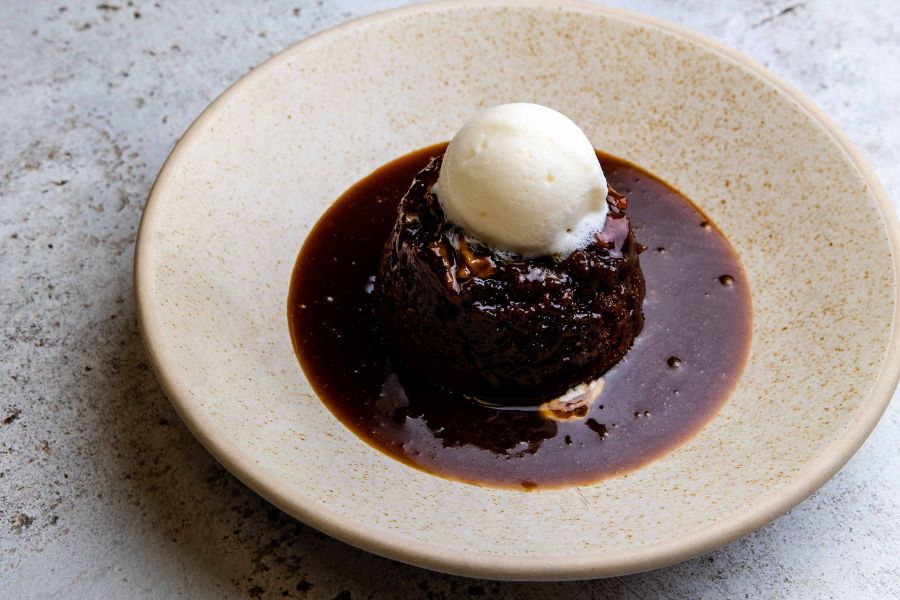 Sticky toffee pudding with ice cream served in a ceramic dish.