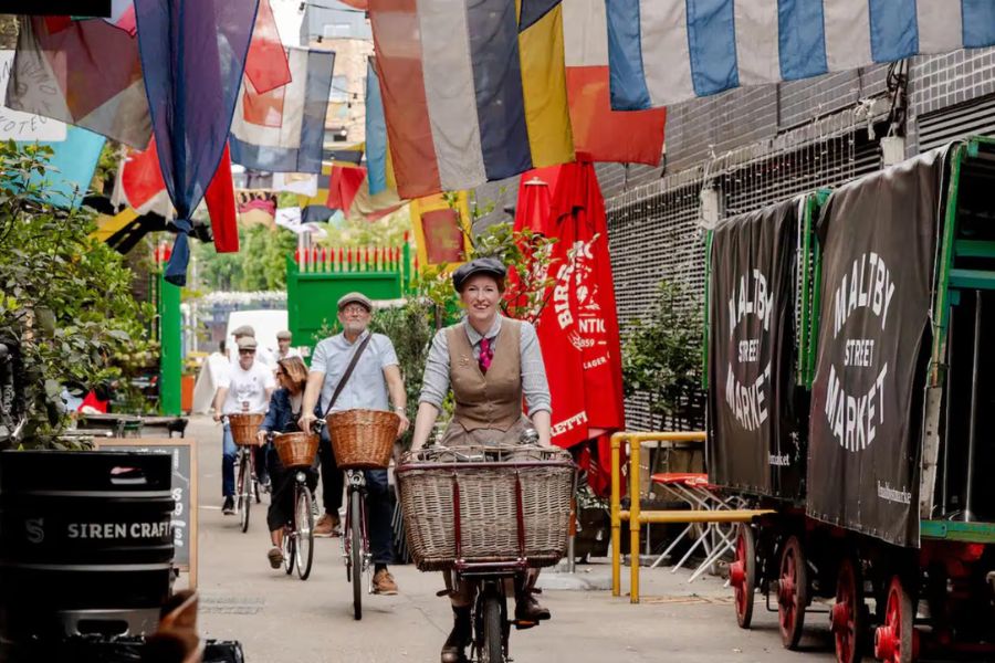 Cyclists riding through Maltby Street Market in London under colorful hanging bunting