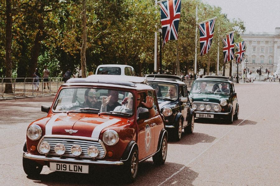 Convoy of classic Mini Coopers driving down The Mall in London with Union Jack flags lining the route