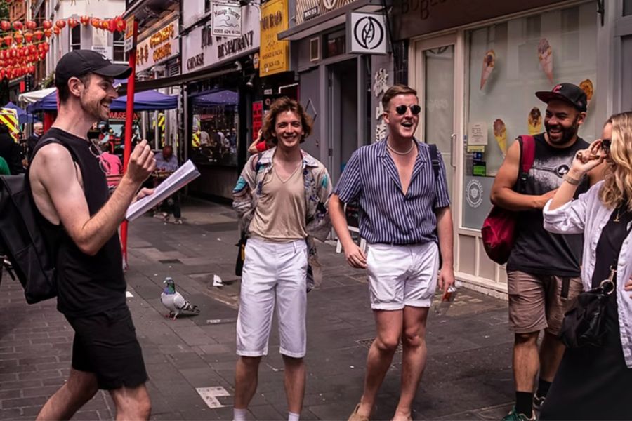 Tour guide leading a group of laughing visitors through London's Chinatown decorated with red lanterns