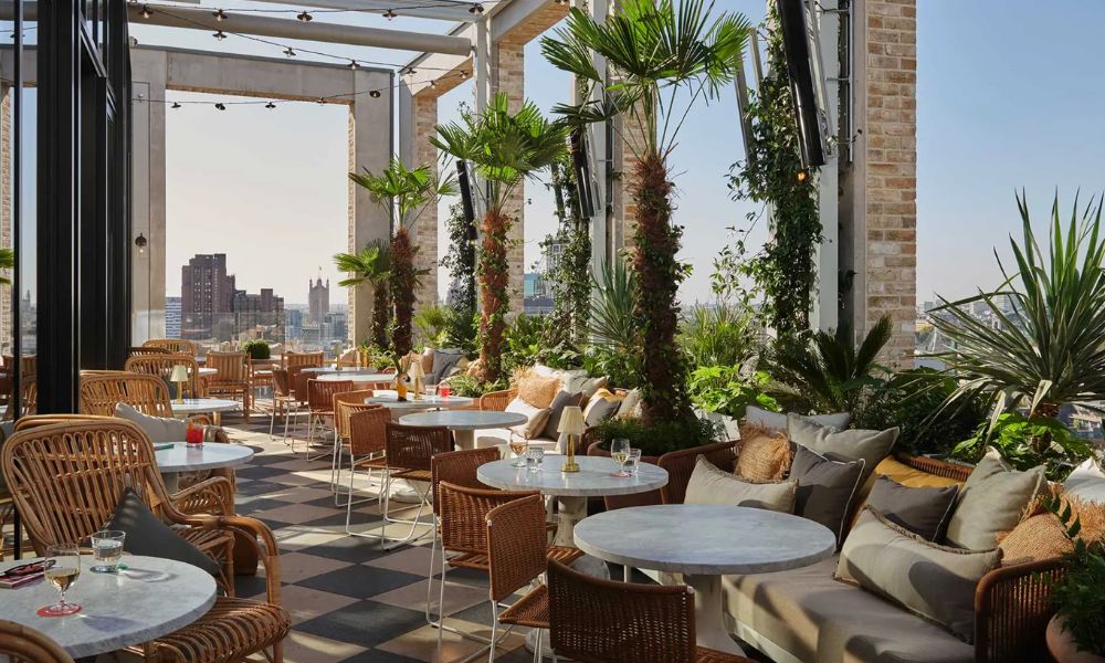 This is an image of a really lovely rooftop filled with plants and lovely tables and cushioned seating.
