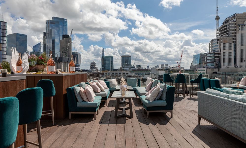 This is an image of an open-air rooftop with a large deck and plenty of sitting furniture and more.