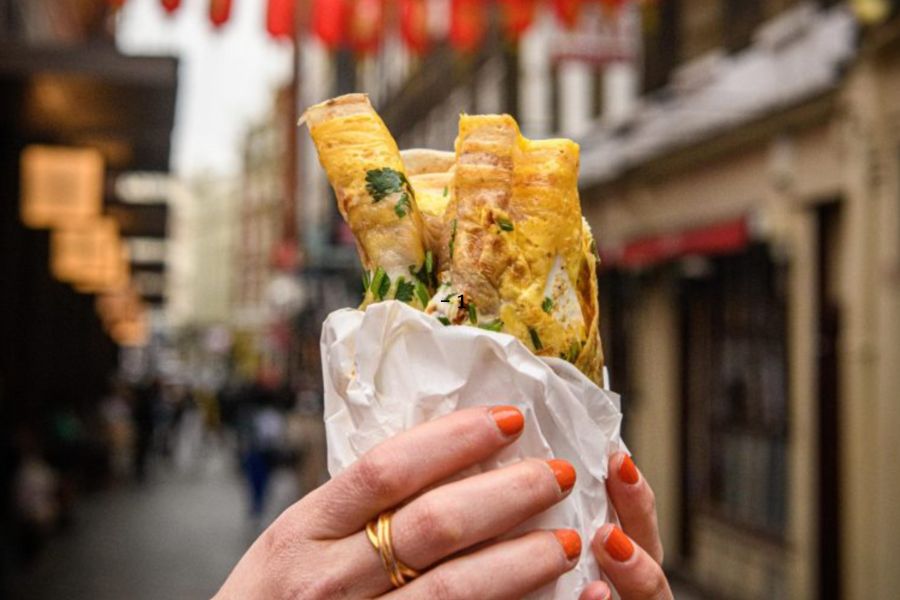 This is an image of a person holding up a Chinese pancake in the middle of Chinatown.