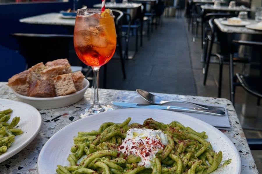 This is an image of a bowl of pasta with an aperol spritz on the side.