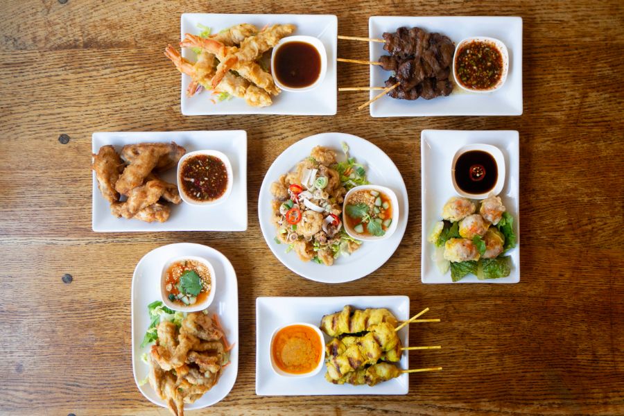 This is an image of a bunch of small thai plates including chicken skewers, prawns, fried chicken and more.