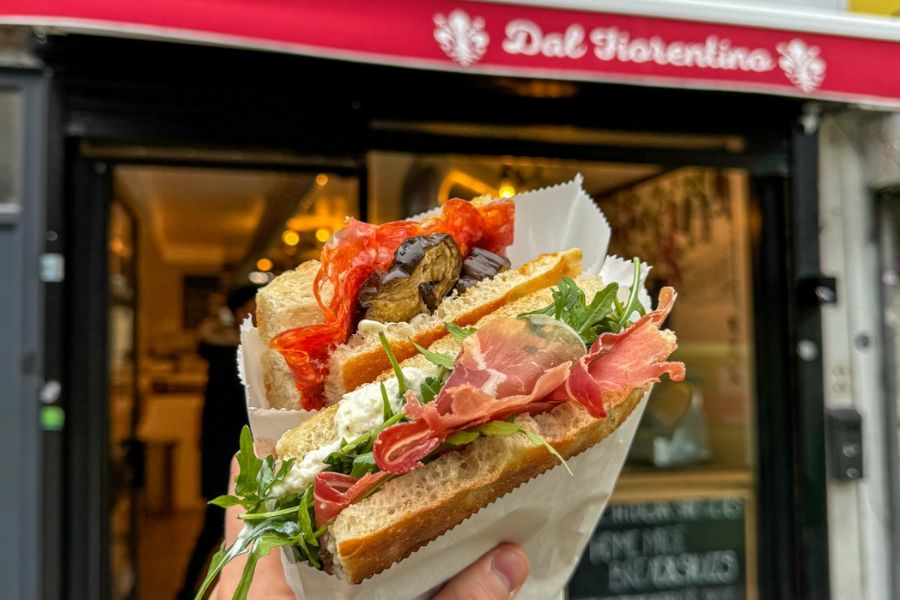 This is an image of a sandwich with prosciutto and aubergine in front of the Dal Fiorentino shop front.