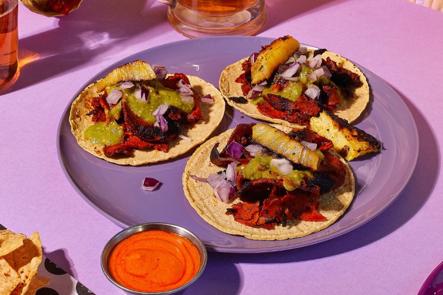 This is an image of three tacos on a purple plate with some sauce.
