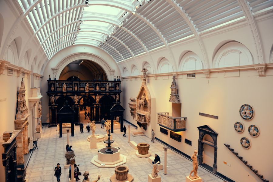 Interior of a grand museum gallery with a vaulted glass ceiling, classical sculptures and visitors exploring the space