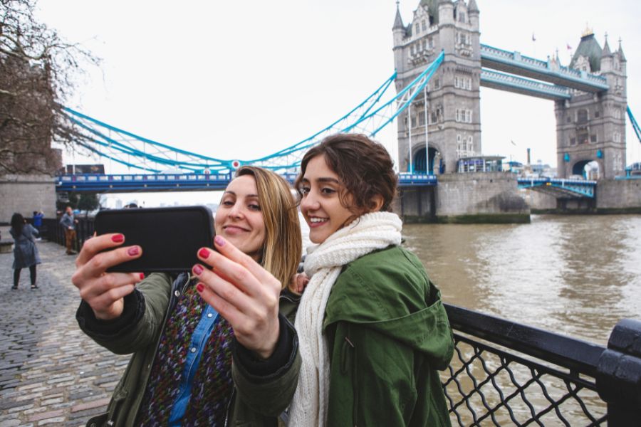 Friends taking a selfie with the Tower Bridge from a hidden spot included in our London itinerary