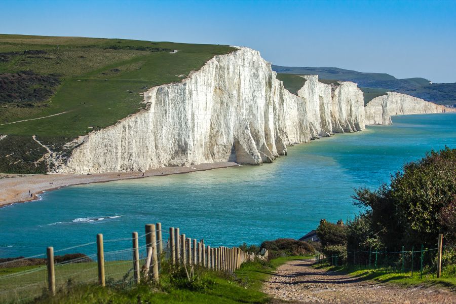 A sweeping aerial view of the Seven Sisters white chalk cliffs along the East Sussex coastline, with turquoise water below and rolling green hills above