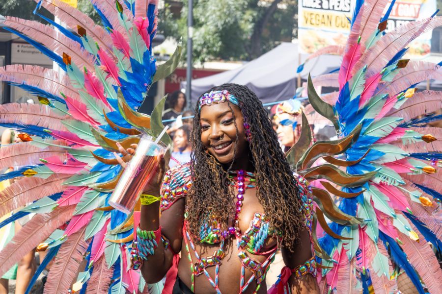 A carnival performer at Notting Hill Carnival wearing an elaborate costume of large pink and blue feathered wings and jewelled accessories