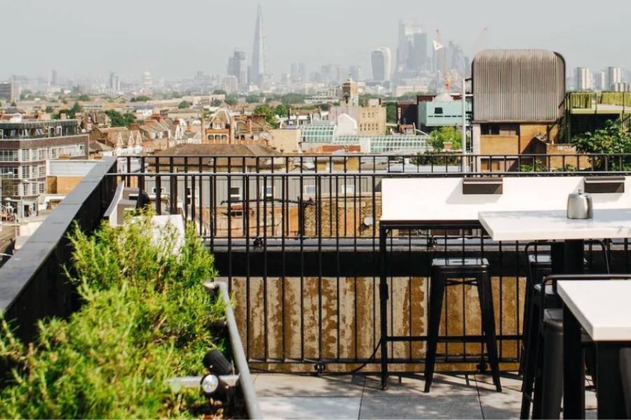 An empty rooftop bar terrace in Peckham with high tables and bar stools, with a sweeping view of the London skyline including the Shard in the distance