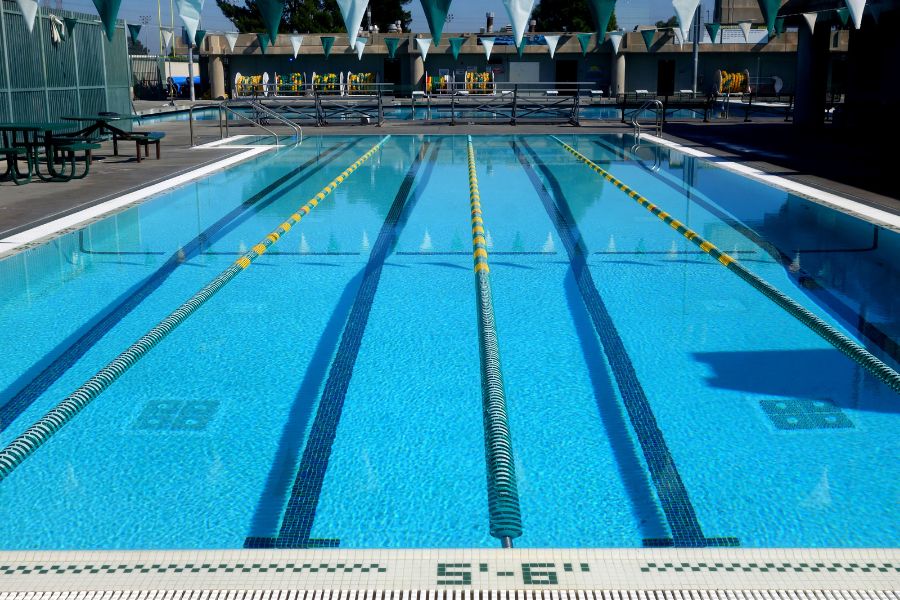 An outdoor swimming pool with clearly marked lanes and lane ropes, surrounded by seating areas on a sunny day