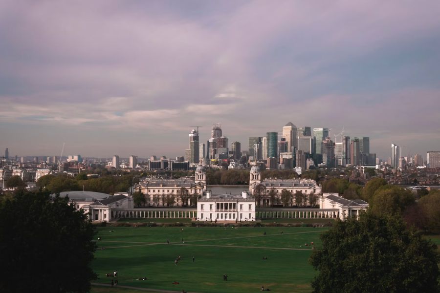 A sweeping view of London's skyline from Greenwich Park, with the Old Royal Naval College in the foreground and the Canary Wharf skyscrapers in the distance