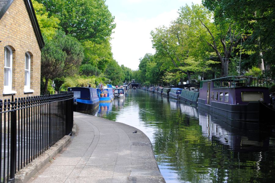 A tranquil stretch of Regent's Canal in Little Venice, lined with colourful narrowboats on both sides and overhanging trees