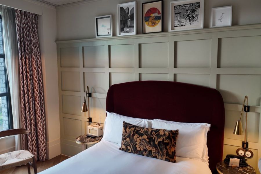 This is an image of a bed with paintings on the wall, and white sheets.