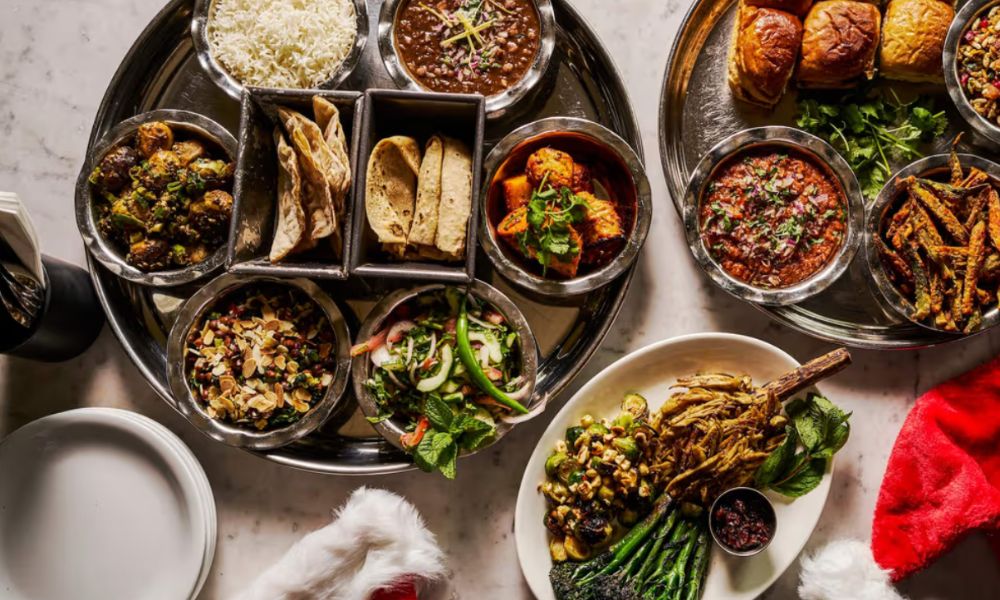 This is an image of a big plate of Indian food on silver trays with santa hats laid on the corner of the table.