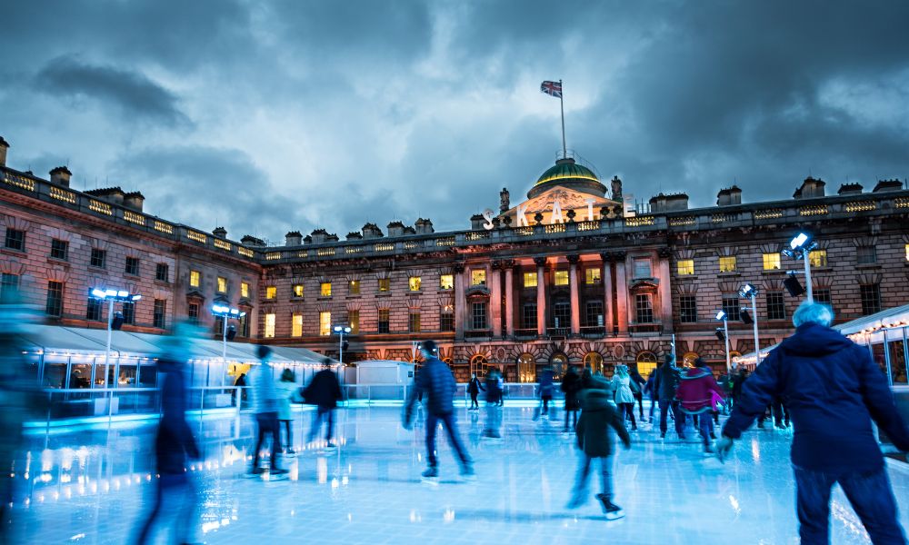 This is an image of Somerset House set up for the ice rink season. There are people gliding around and cute Christmas lights around.