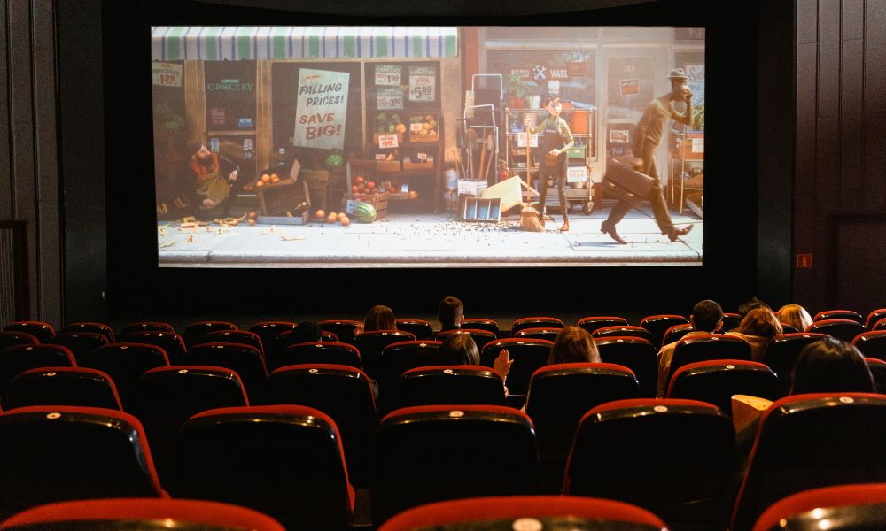 This is an image of a theatre with red seats and a projector with a movie on at the front.
