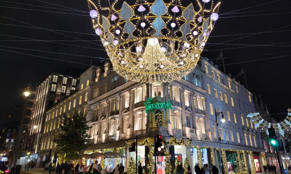 This is an image of a big department store with people crowded around the front and a big light fixture in the middle of the street.