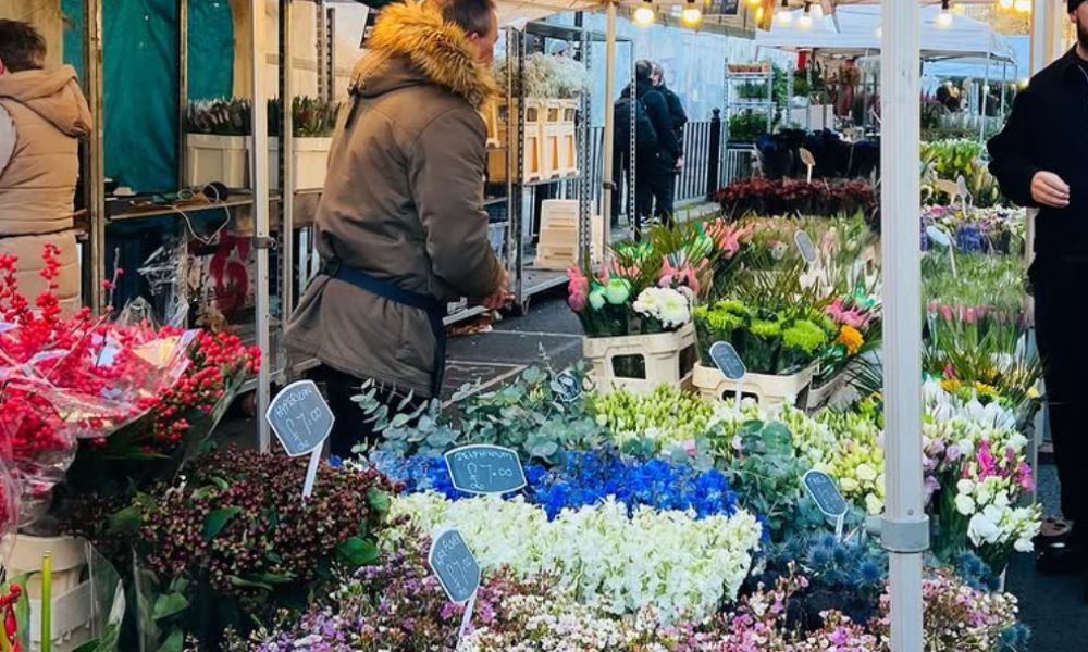 This is an image of a flower stall full of plenty of different flowers with a man working to serve customers.