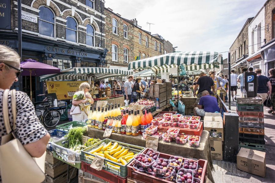 Customers purchasing fresh fruits and vegetables on a sunny day at Broadway market.