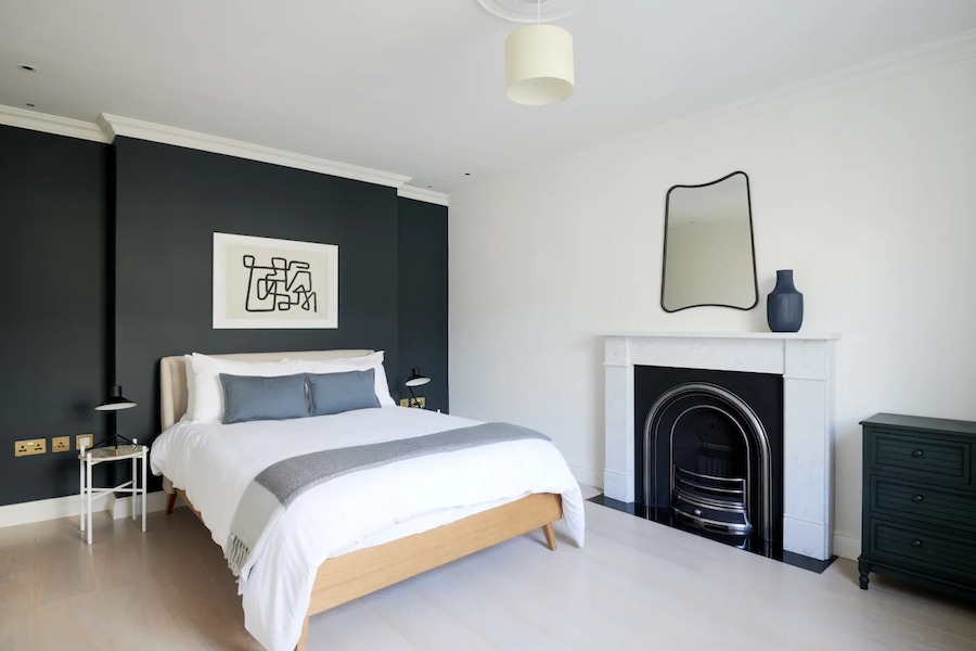 This is an image of a sleek and minimalistic bedroom with a double bed, fireplace and clean walls and flooring.