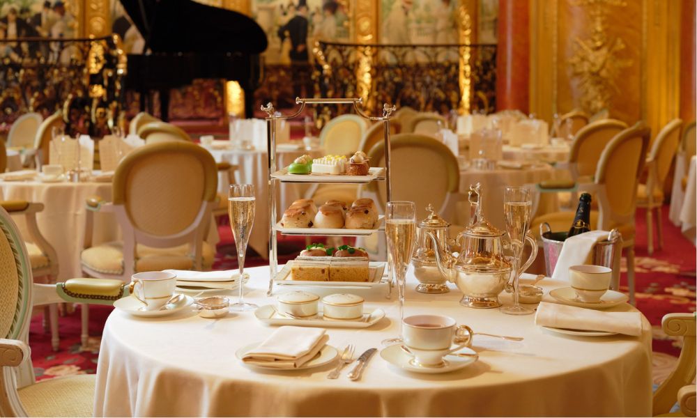 This is an image of a round table that has been set with nice crockery and cutlery. In the middle is a three-tiered afternoon tea stand, as well as flutes of champagne.