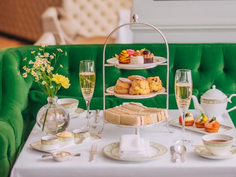 This is an image of a nice afternoon tea spread with a three-tiered cake stand, teapot and champagne flutes.