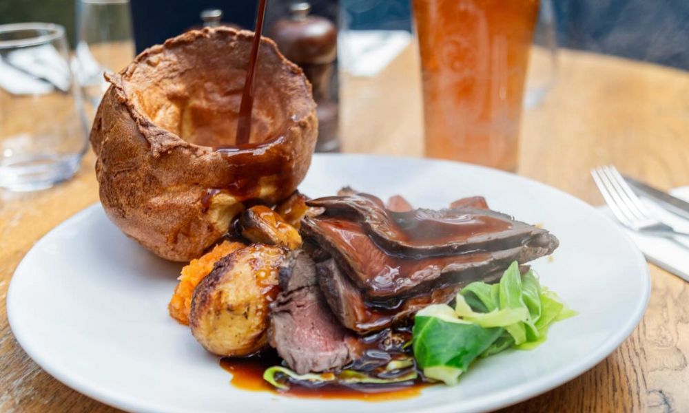 This is an image of a roast beef with someone pouring gravy into a Yorkshire pudding.
