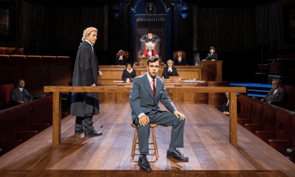 This is an image of a man sitting in the middle of a courtroom with a jury and judge behind him.