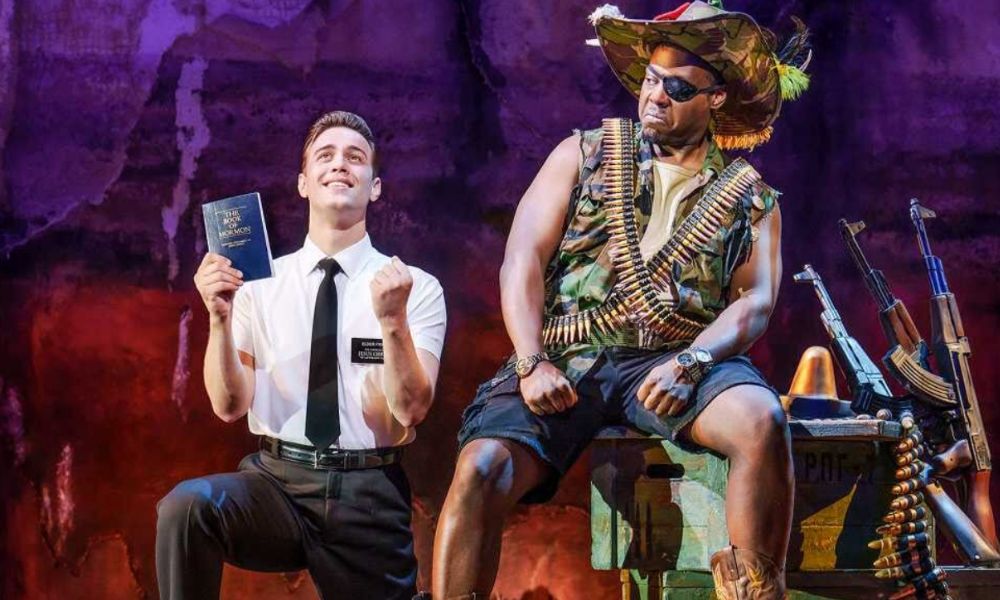 Best West End shows in London: This is an image of a mormon on his knees with the Bible clenching his fists in happiness, while a soldier wearing a round of bullets sits next to him looking at him in disgust.
