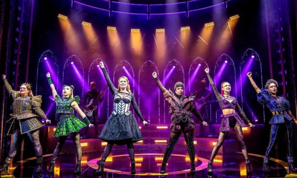 This is an image of Henry's six wives all dancing in the middle of the stage with their fingers pointing into the air.