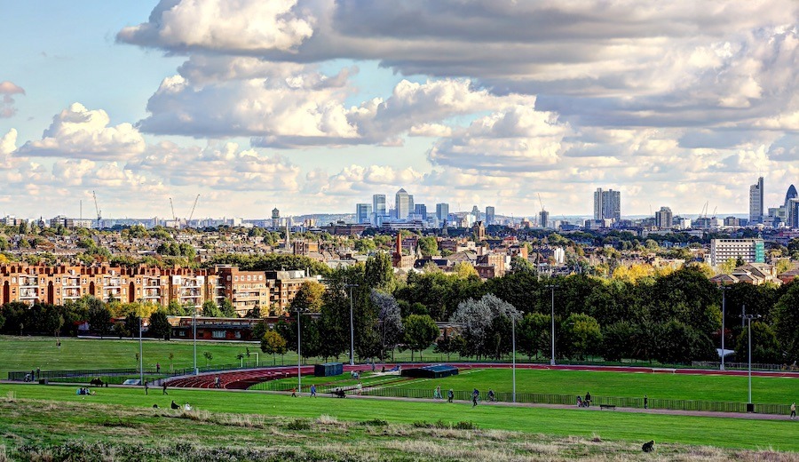 View of the London skyline at the edge of Hampstead Heath. Long green grass with building seen in the horizon. Staying further out of the city centre is a great way to save on your London accommodation.