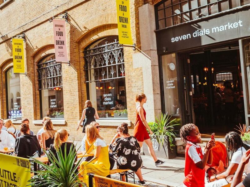 This is an image of the outside of Seven Dial's Market where there is seating and people sitting around eating together.