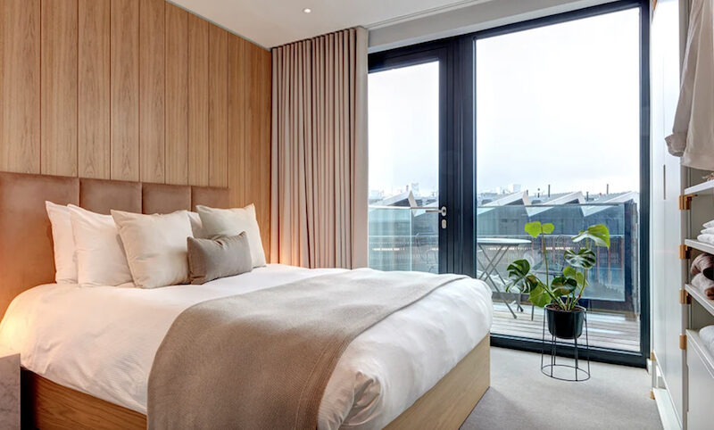 This is an image of a sleek hotel bedroom with big windows and a muted palette.