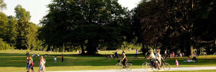 This is an image of a big park with lots of greenery around and people walking or cycling.