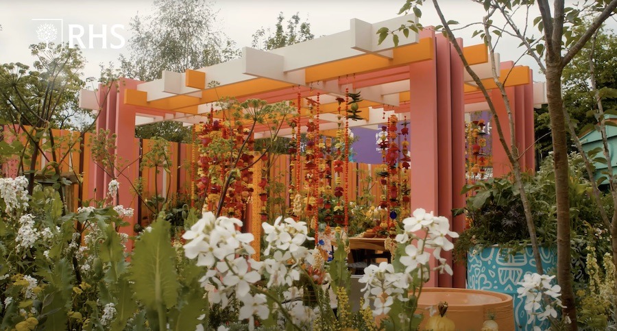 The picture shows a garden with beautiful flowers and a colourful structure in the back. 