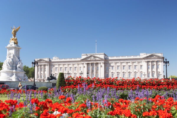 This is an image of the front of a palace in London with white walls, blue skies, and a beautiful garden in front.