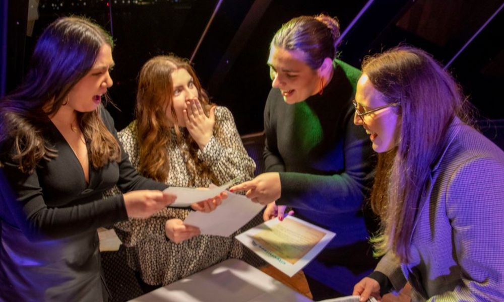 This is an image of a group of people laughing together in shock of what's on the piece of paper in front of them.