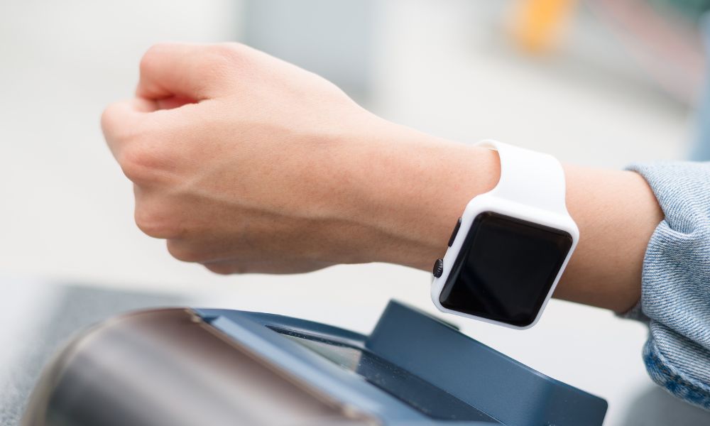 This is an image of a person tapping their contactless Apple watch card on a machine.