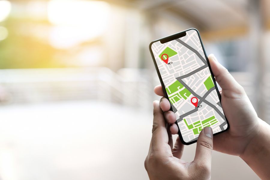 Hands holding a smartphone displaying a navigation map app with two red location pins marking points on a street map.