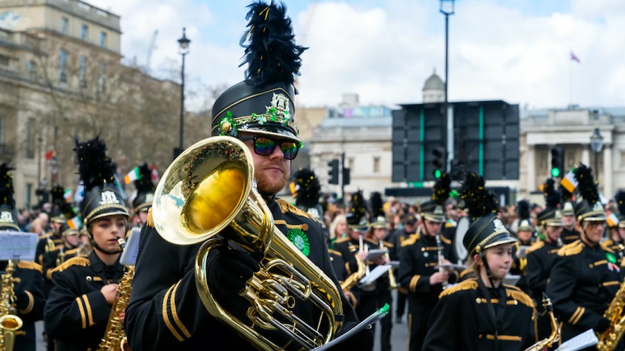 This is an image of a man holding a saxophone surrounded by other musicians at a parade in London for St Patrick's day. They are dressed in smart uniforms with hats and polished brass instruments.