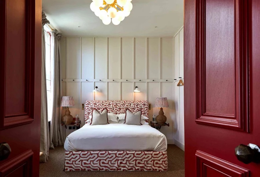 This is an image of a hotel bedroom with a double bed, red doors and a neutral coloured carpet on the floor.