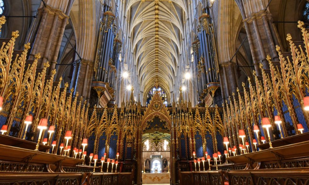 This is an image of the inside of Westminster Abbey with its tall ceilings, rows of pews and stained glass windows.
