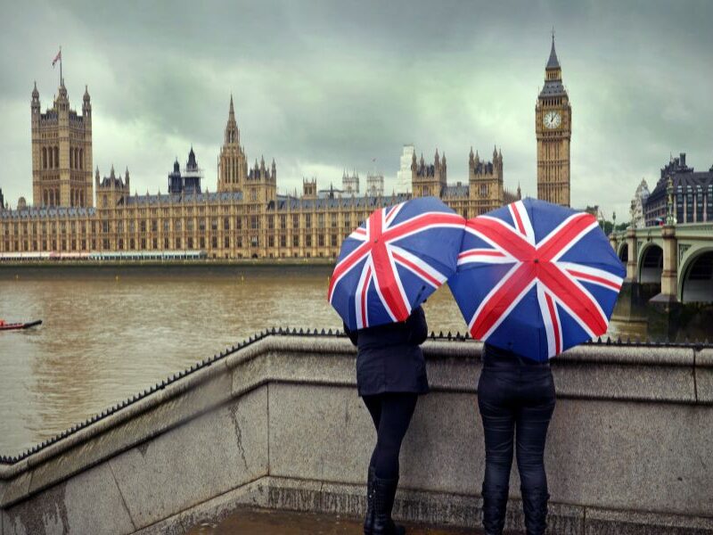 This is an image of people with British umbrellas staring off into the distance where Big Ben and the Houses of Parliament.