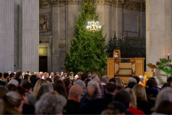 This is an image of the inside of St Paul's Cathedral with lots of people sitting in pews and a big Christmas tree in the background.