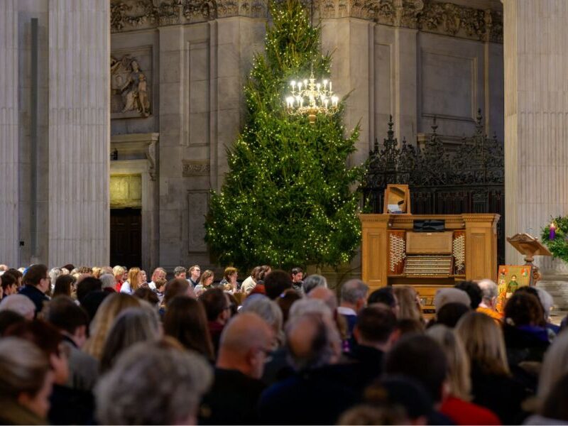 This is an image of the inside of St Paul's Cathedral with lots of people sitting in pews and a big Christmas tree in the background.
