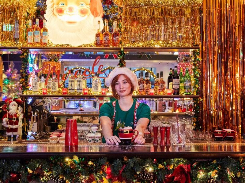 This is a picture of the Miracle Christmas-themed cocktail bar at Henrietta Hotel where the whole bar is lit up with decorations and the bartender is in an elf costume.